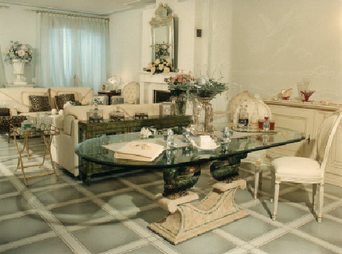 Credenza in legno massello laccata in bianco e oro antico, sedie in stile Luigi XVI in tessuto capiton�e, tavolo ovale con piano in 
cristallo.